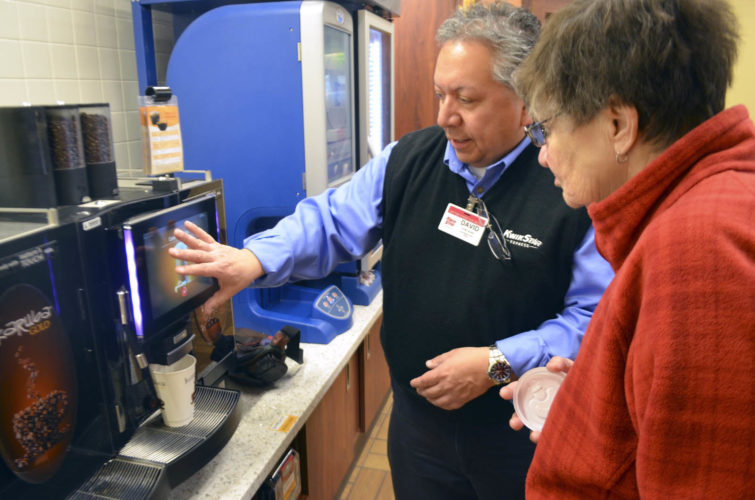 -Messenger photo by Joe Sutter Store Leader David Munoz shows Mary Ellen McGough how to work the Karub Gold machine, which grinds its own espresso beans and mixes drinks with real milk and optional flavors added in.